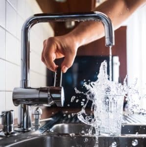 Person aggressively filling up a glass of water at the kitchen sink while water splashes everywhere