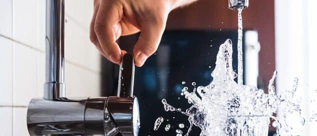 Person aggressively filling up a glass of water at the kitchen sink while water splashes everywhere