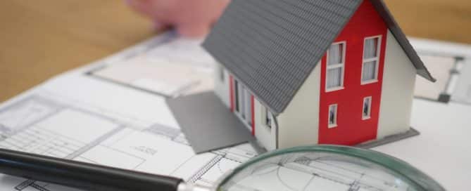 House, magnifying glass, and toy pig on top of floor plan
