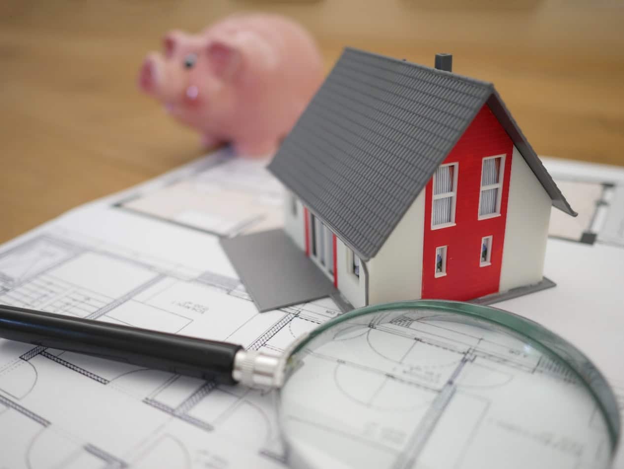 House, magnifying glass, and toy pig on top of floor plan