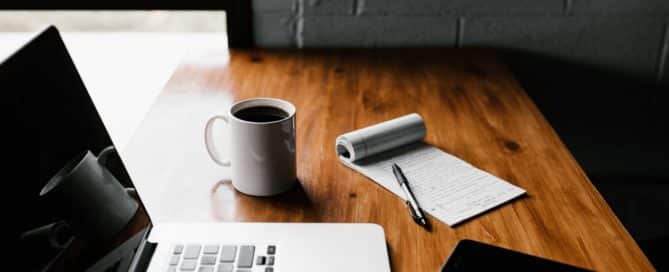 laptop, note pad, coffee, and phone on a desk