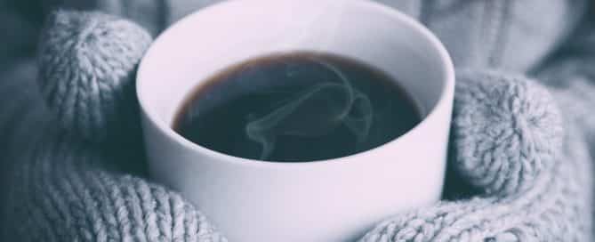 person wearing mittens holding a hot drink