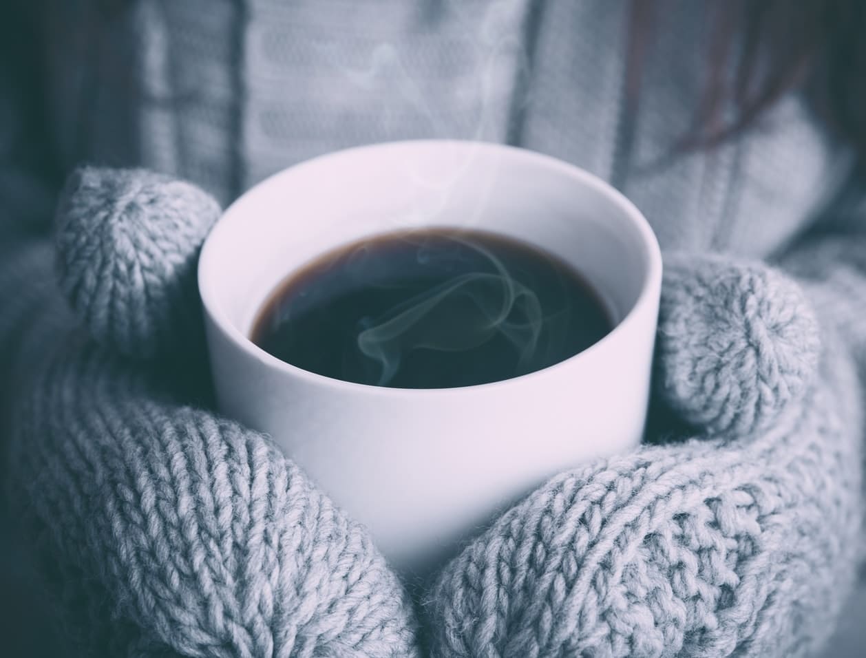 person wearing mittens holding a hot drink