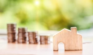 Wooden house cutout in front of decreasing stacks of coins