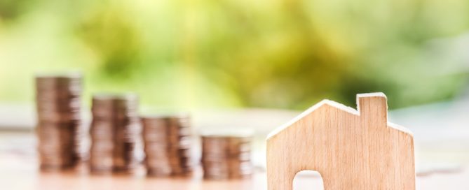 Wooden house cutout in front of decreasing stacks of coins