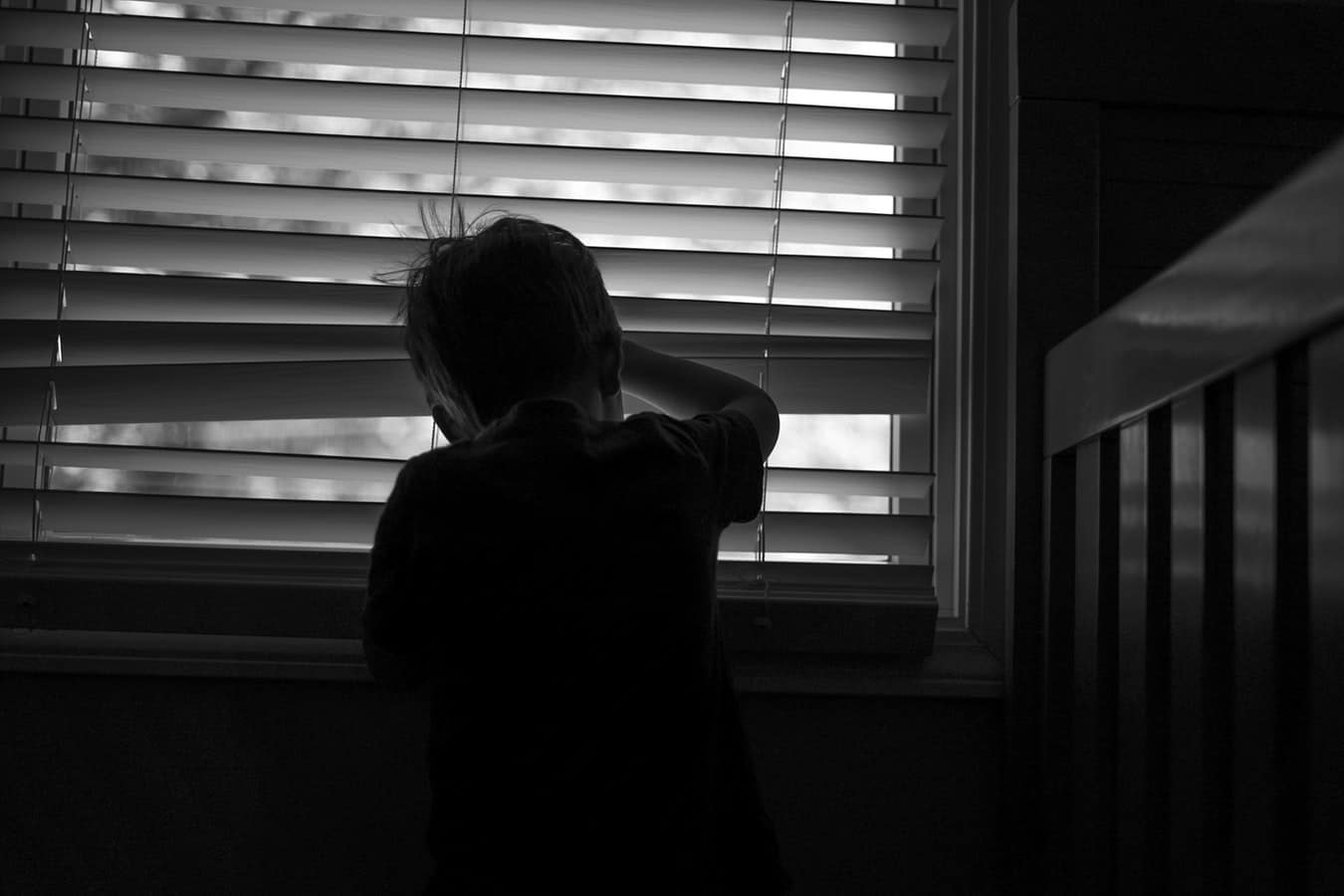Black and white image of a child peaking through the blinds