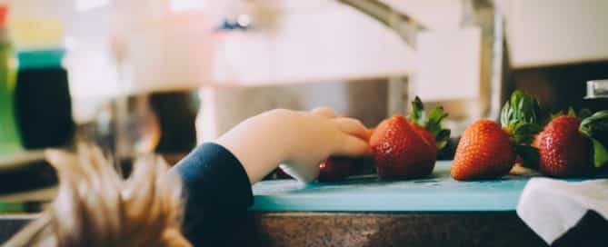 child reaching for a strawberry on the kitchen counter