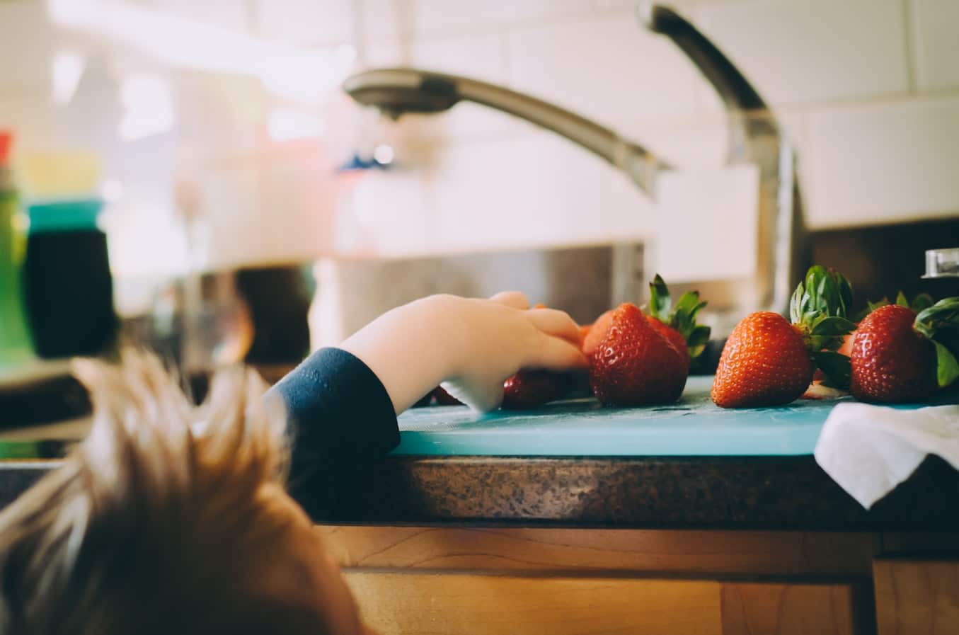 child reaching for a strawberry on the kitchen counter