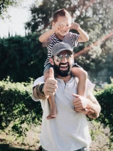 Man giving thumbs up with child on his shoulders