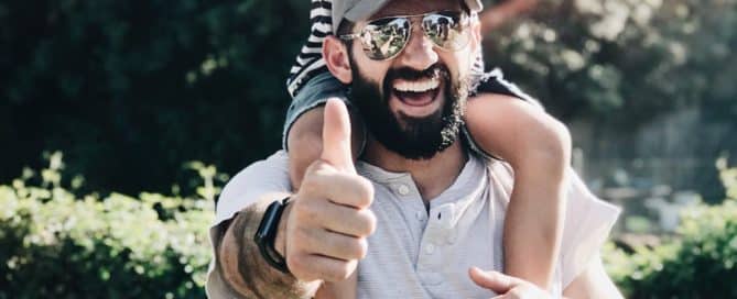 Man giving thumbs up with child on his shoulders