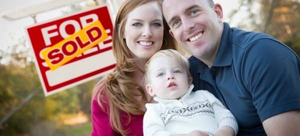 Couple with baby sitting next to a "Sold" For Sale sign