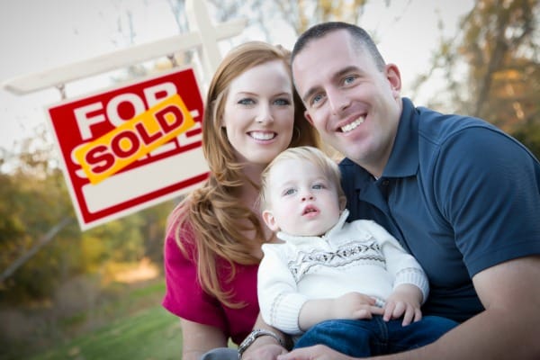 Couple with baby sitting next to a "Sold" For Sale sign