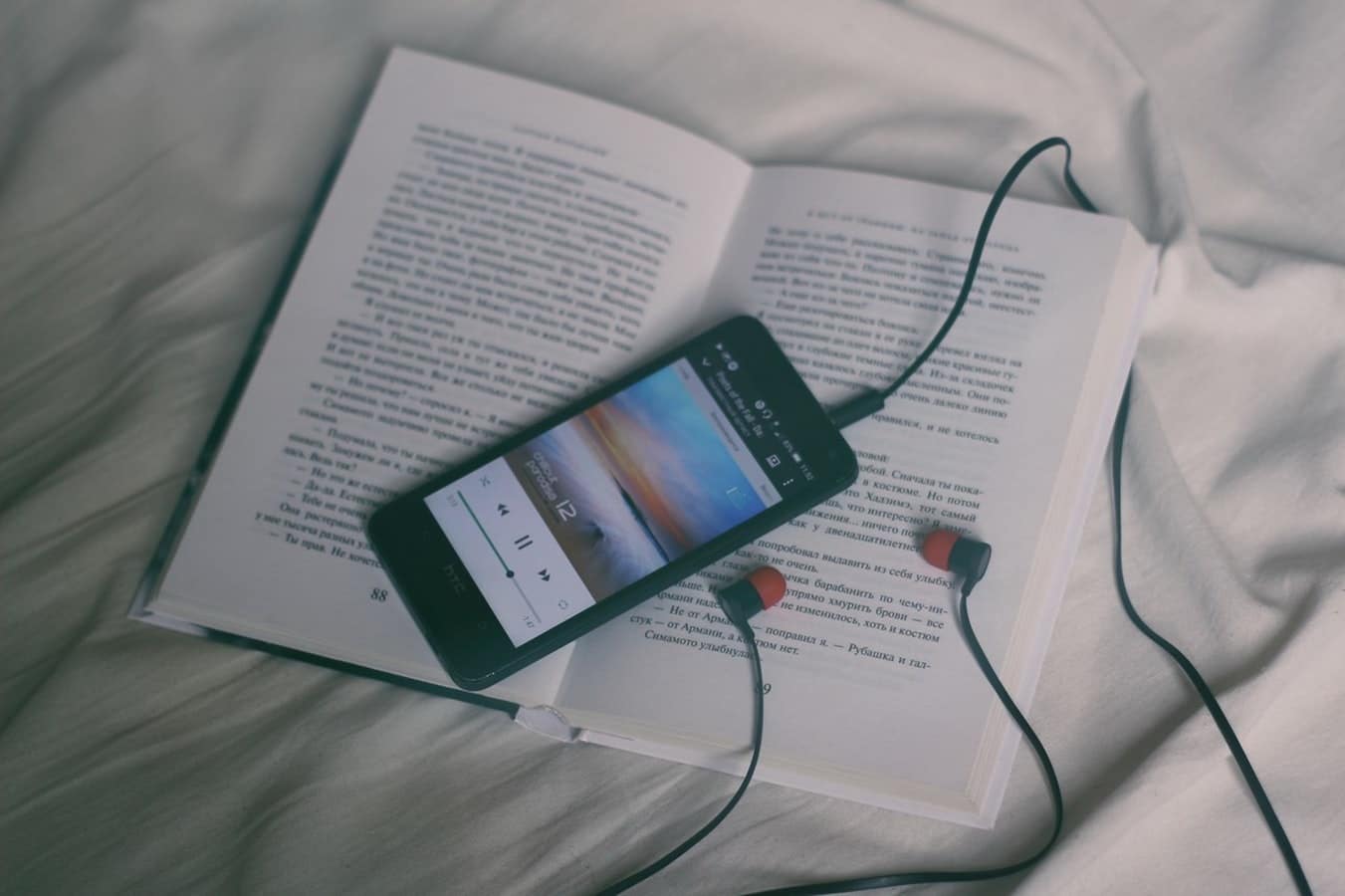 Smart phone playing music, with headphones plugged in, wrapped around a book